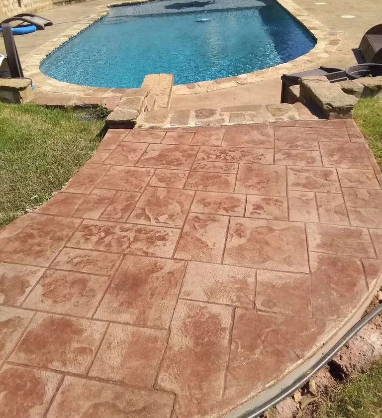 Pool surrounded by red stamped concrete deck